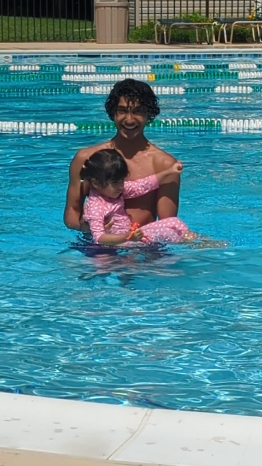 Rehan smiling as he holds a toddler in the pool during a lesson
