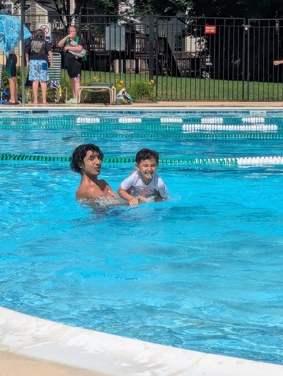 A laughing toddler paddling beside Rehan during a lesson